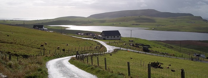Country road running alongside a house on the bank of a body of water