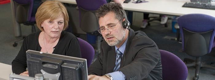 Two people looking at a computer screen. One wearing a headset